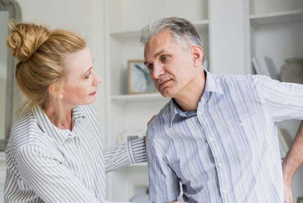 Woman supporting a man experiencing discomfort at home, illustrating the impact of chronic inflammation on daily life.