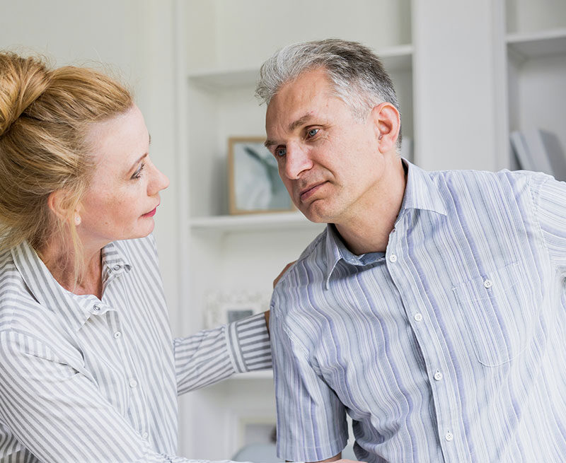 Woman supporting a man experiencing discomfort at home, illustrating the impact of chronic inflammation on daily life.